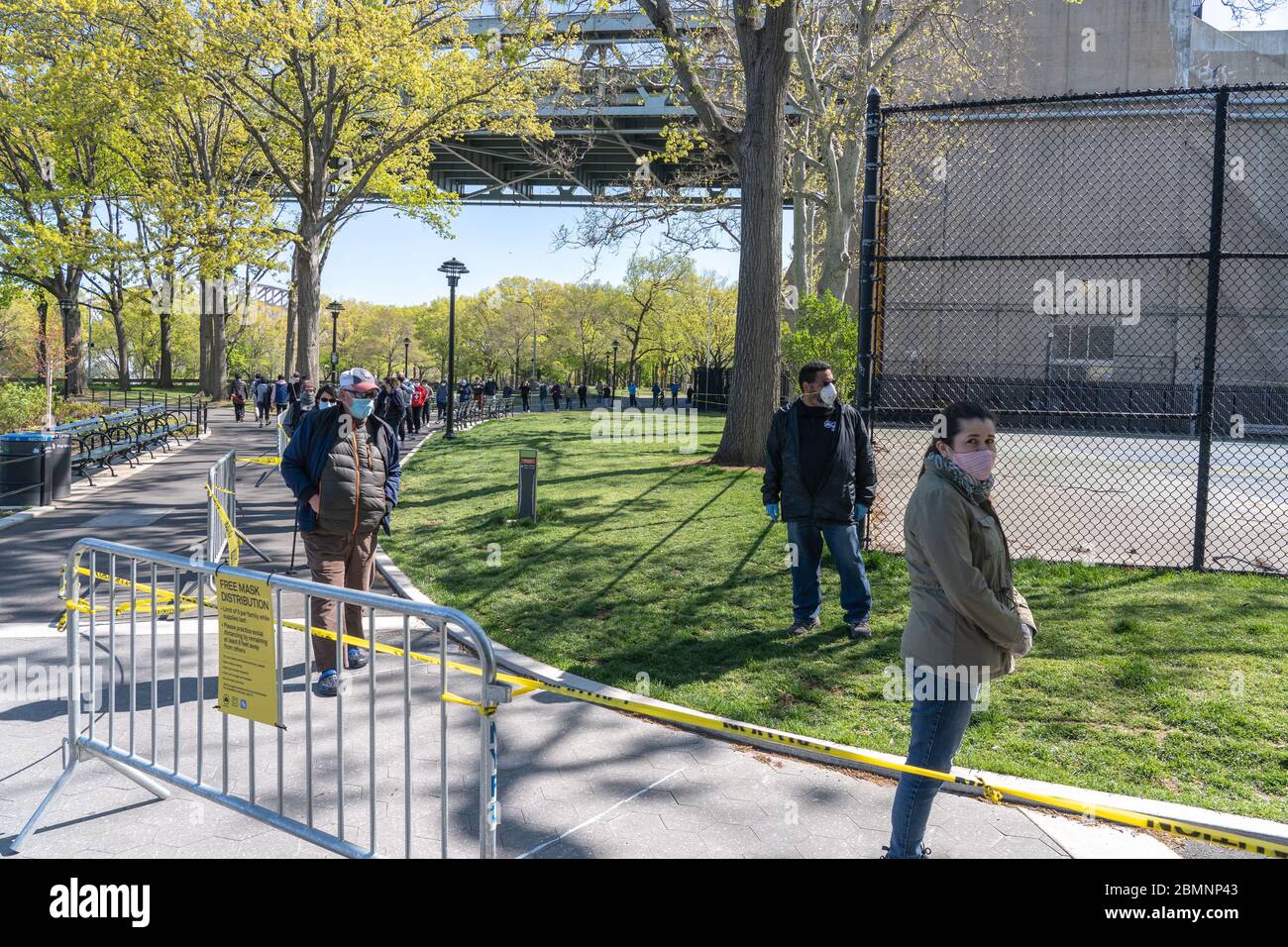 NEW YORK, NY - 10. MAI 2020: Menschen stellen sich in sozialer Distanz für kostenlose Gesichtsmasken aus den NYC Parks im Astoria Park inmitten der Covid-19-Pandemie an. Stockfoto