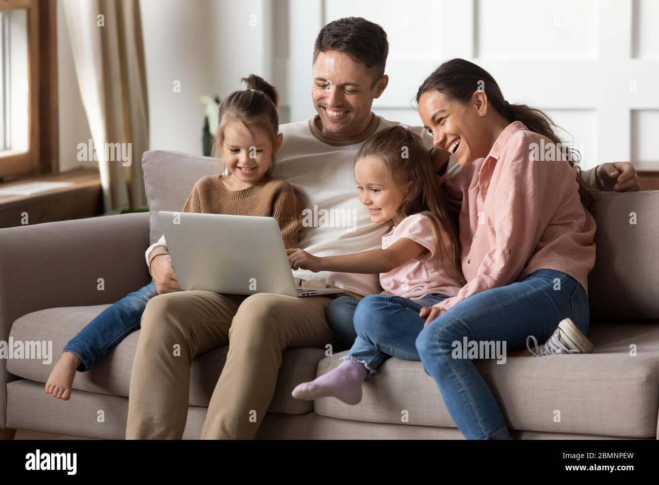 Glückliche Familie mit zwei kleinen Töchtern, die zusammen einen Laptop benutzen Stockfoto