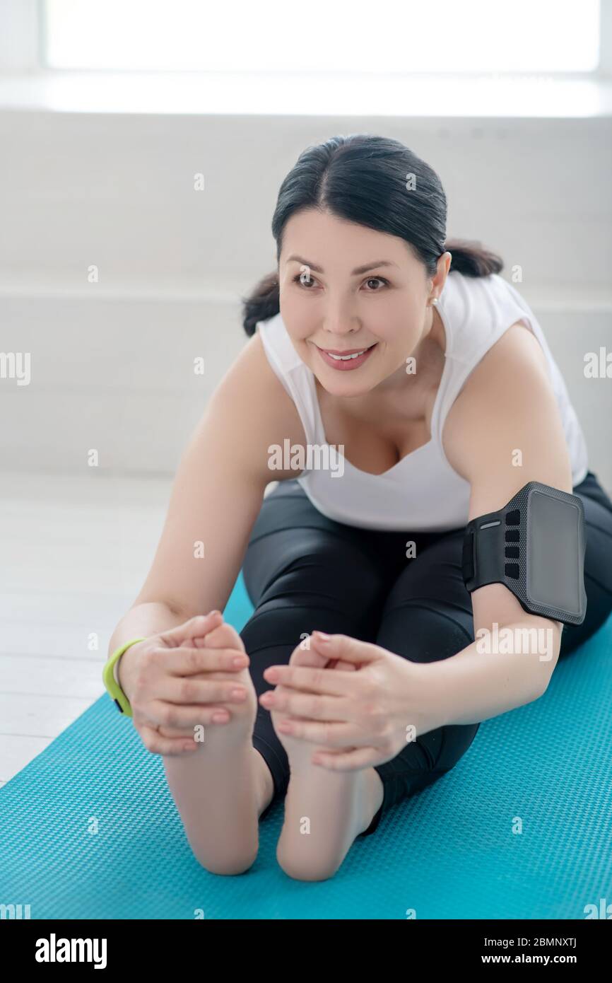 Brunette Frau sitzt auf Teppich, Stretching, lehnt sich nach vorne Stockfoto