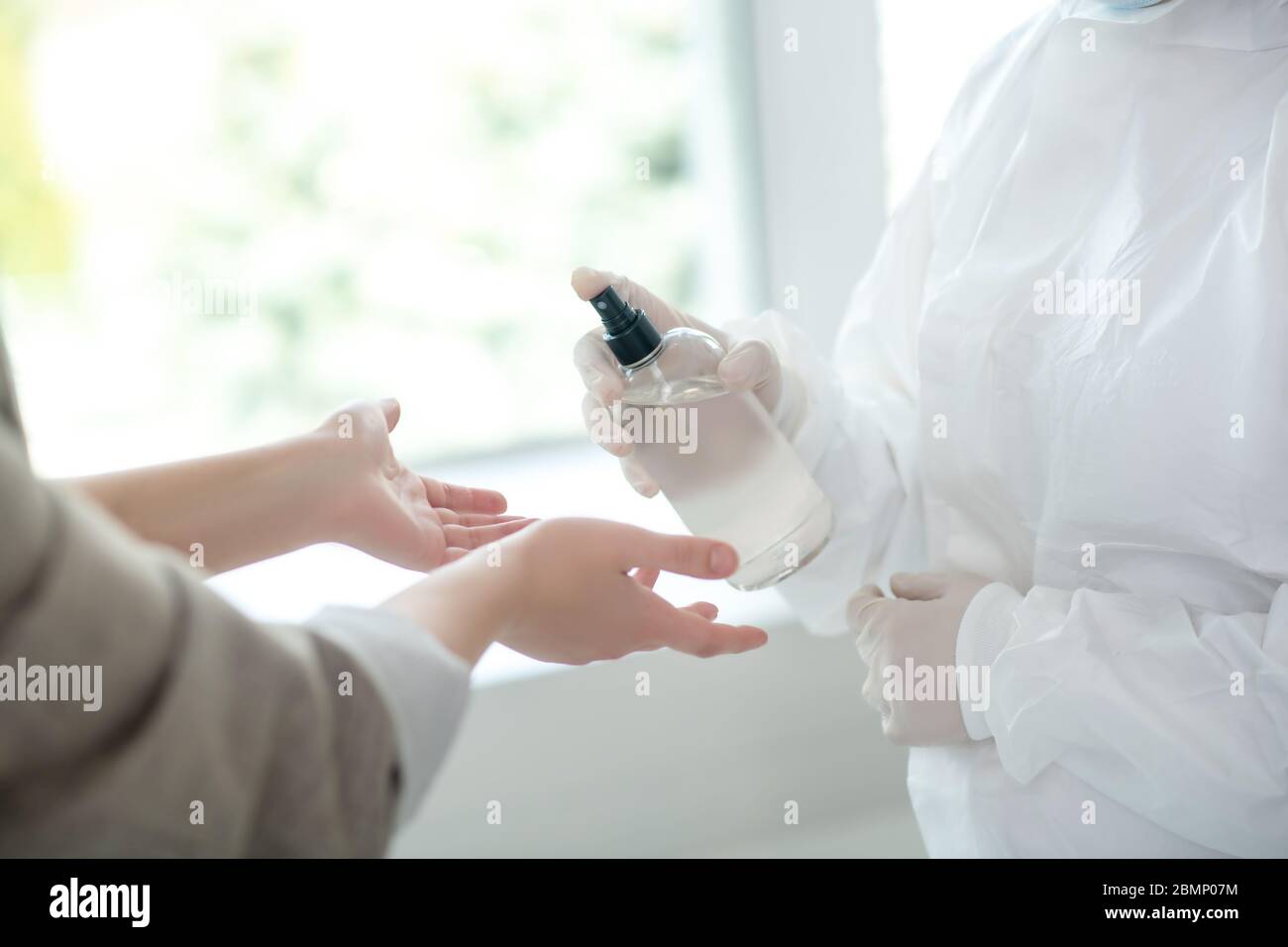 Nahaufnahme der Hände eines Arztes, der antiseptisch auf die weiblichen Hände sprüht Stockfoto