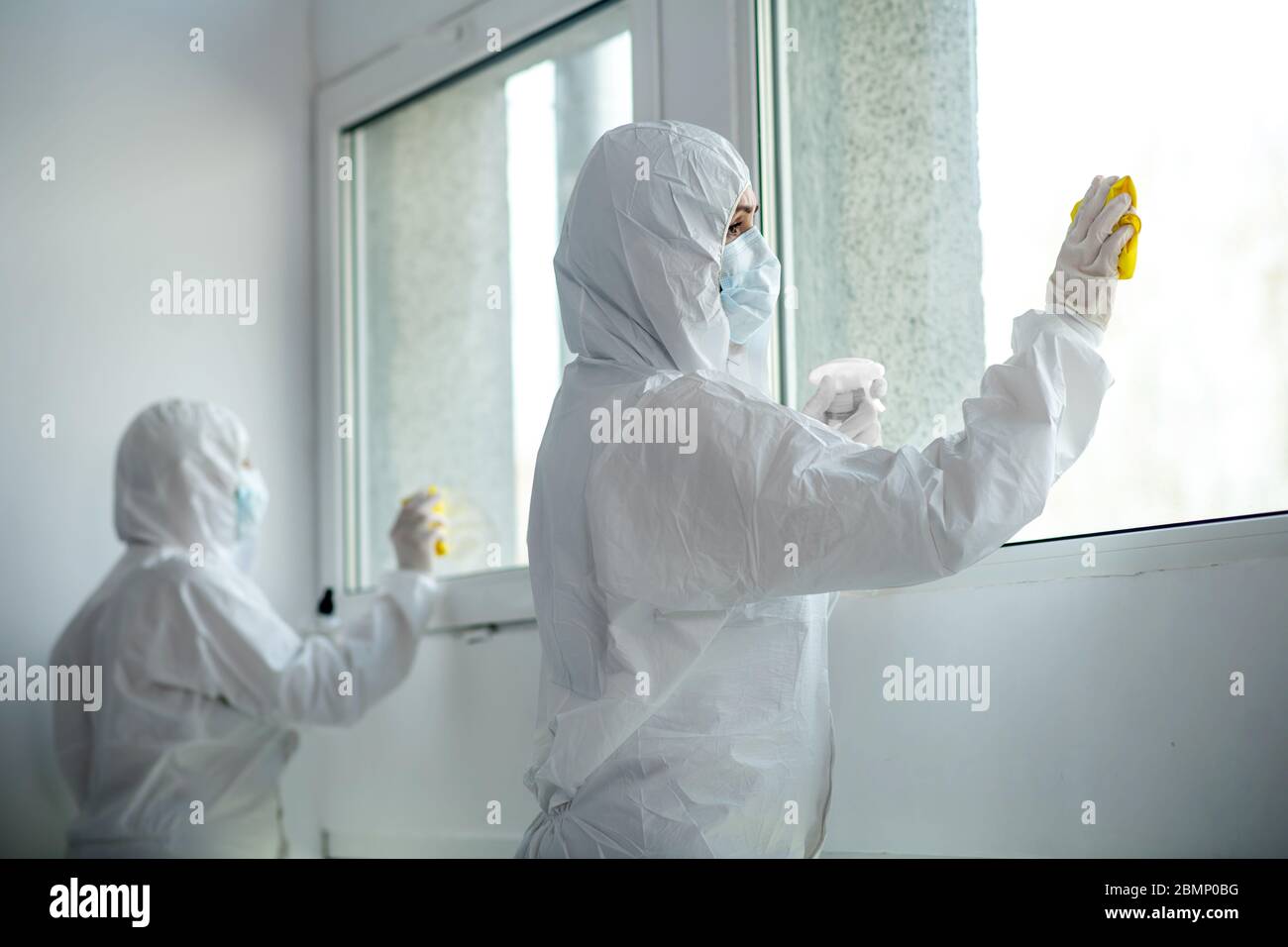 Medizinische Mitarbeiter in Schutzkleidung und medizinische Masken Desinfektion Fenster Stockfoto
