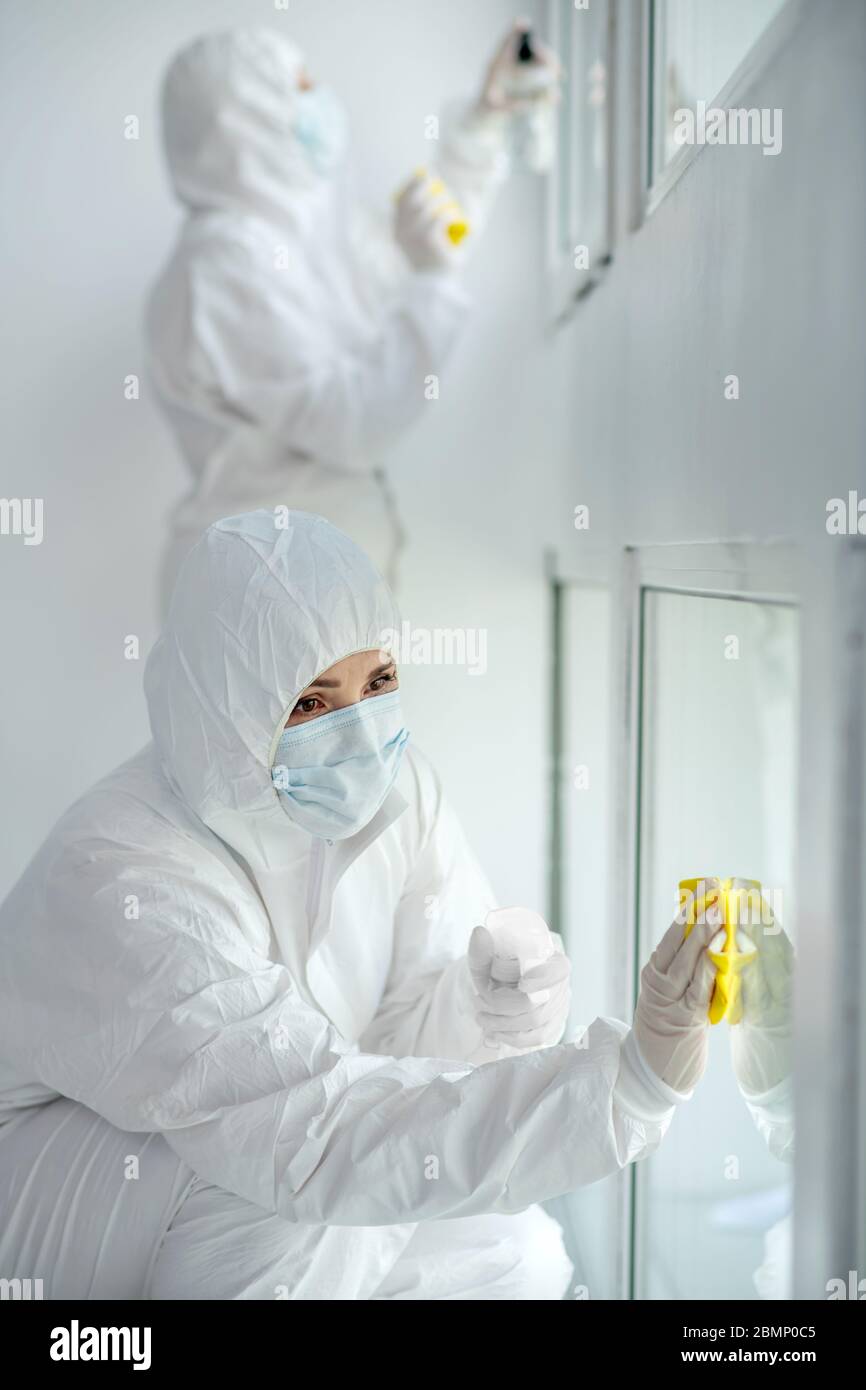 Medizinische Mitarbeiter in Schutzkleidung und medizinische Masken Desinfektion Fenster Stockfoto
