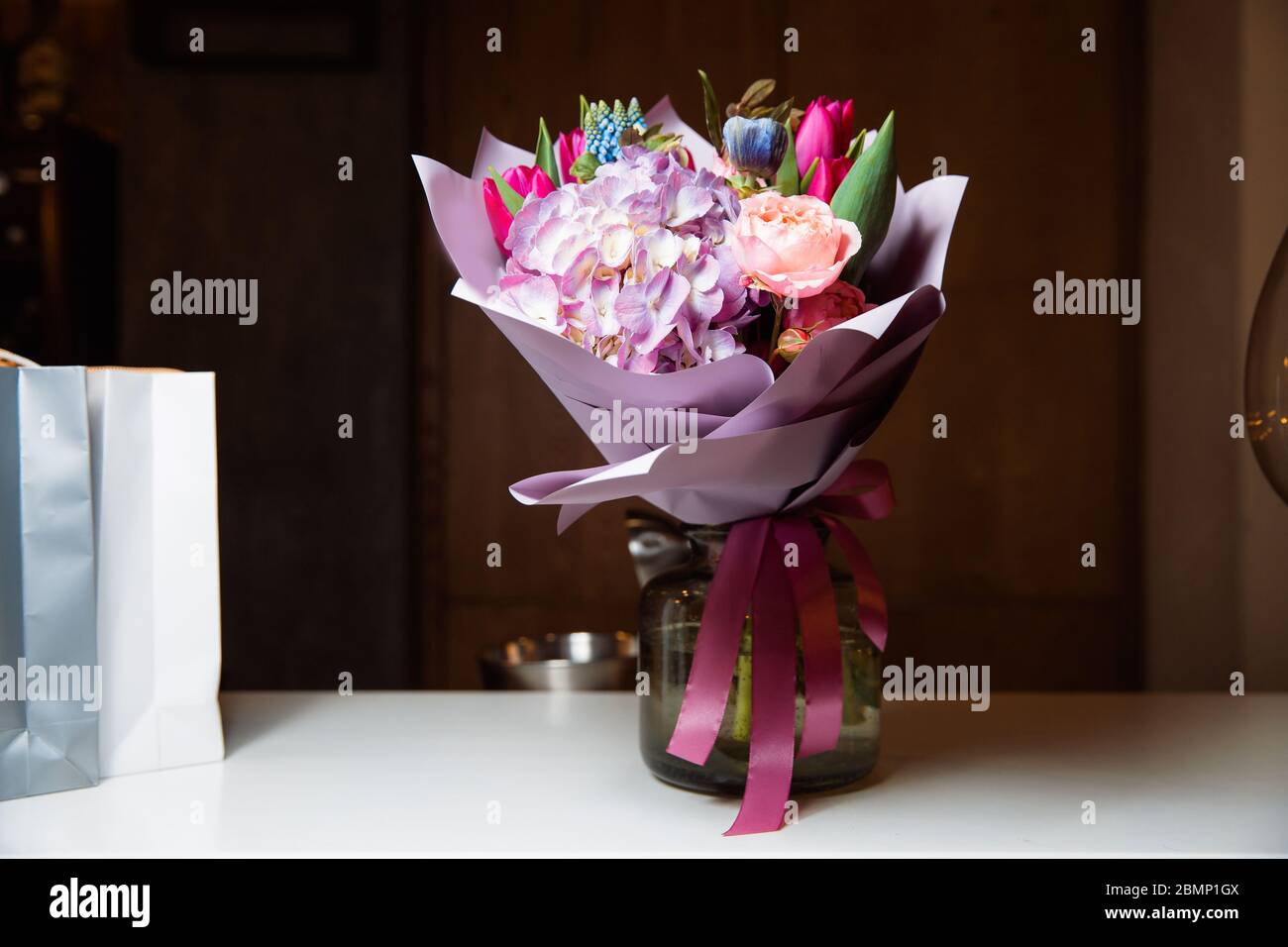 Ein großer Strauß von bunten Blumen verschiedener Art steht in einer transparenten Glasvase. Stockfoto