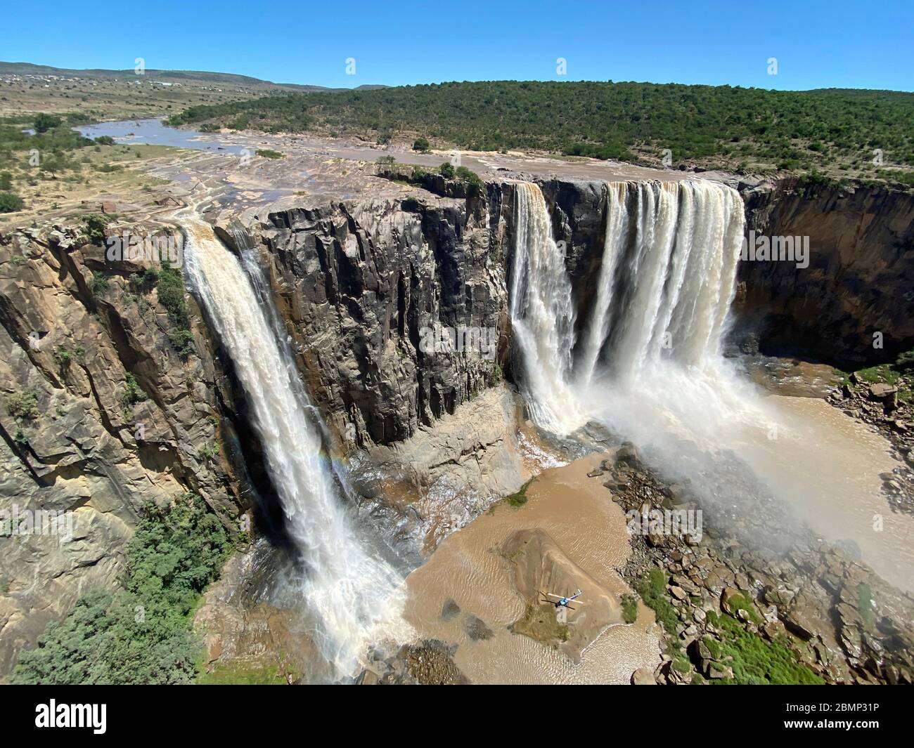 Ein erfahrener Pilot hat seinen Hubschrauber unter dem großen Wasserfall auf einer kleinen Insel abgestellt. Der Kapitän muss wirklich gut im Fliegen sein. Stockfoto