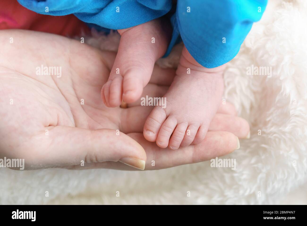 Ein kleiner Kinderfuß in den Händen der Eltern. Pflege eines Neugeborenen Stockfoto
