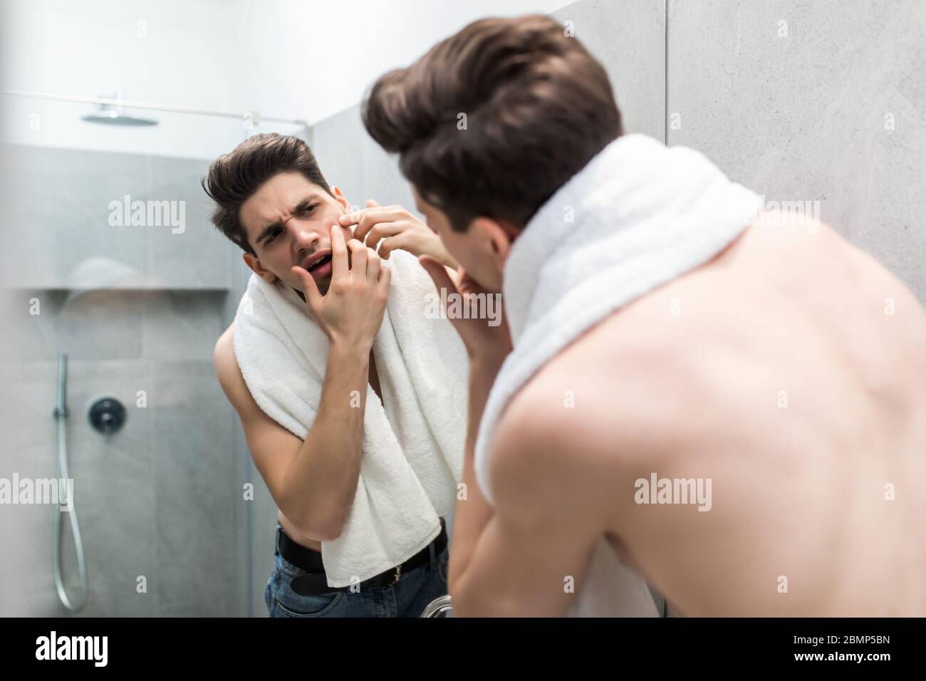 Junger Mann, der vor dem Spiegel steht und sein Gesicht berührt Stockfoto