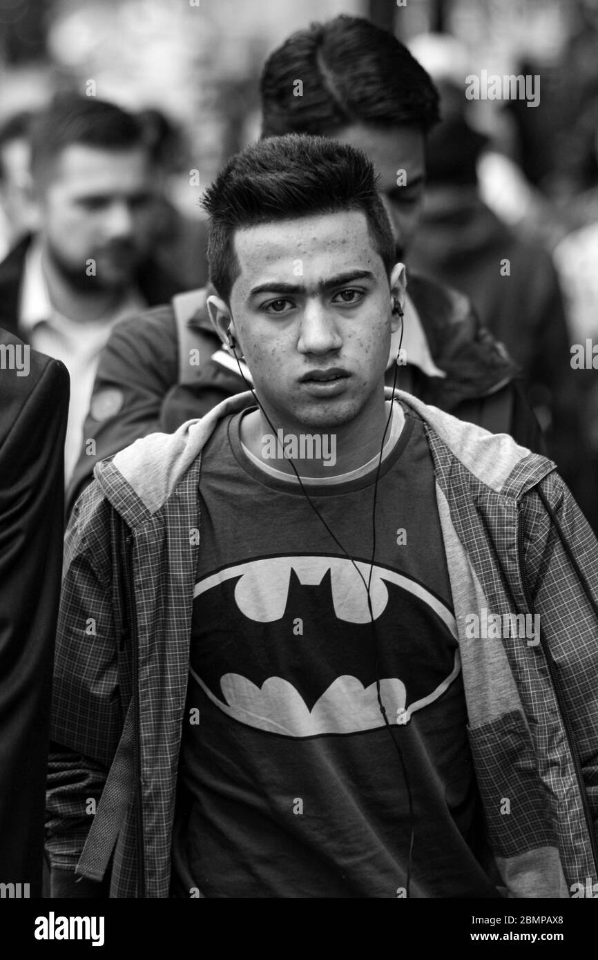 Junger Mann mit Batman-Shirt und kabelgebundenen Ohrhörern in der Menge, der direkt auf die Kamera in London, England, Großbritannien schaut Stockfoto
