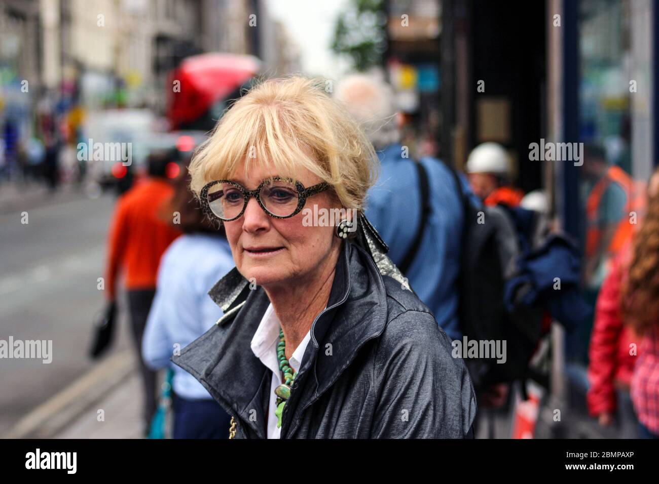 Ältere Frau mit kühnen Brillen auf dem Bürgersteig in London, England Stockfoto
