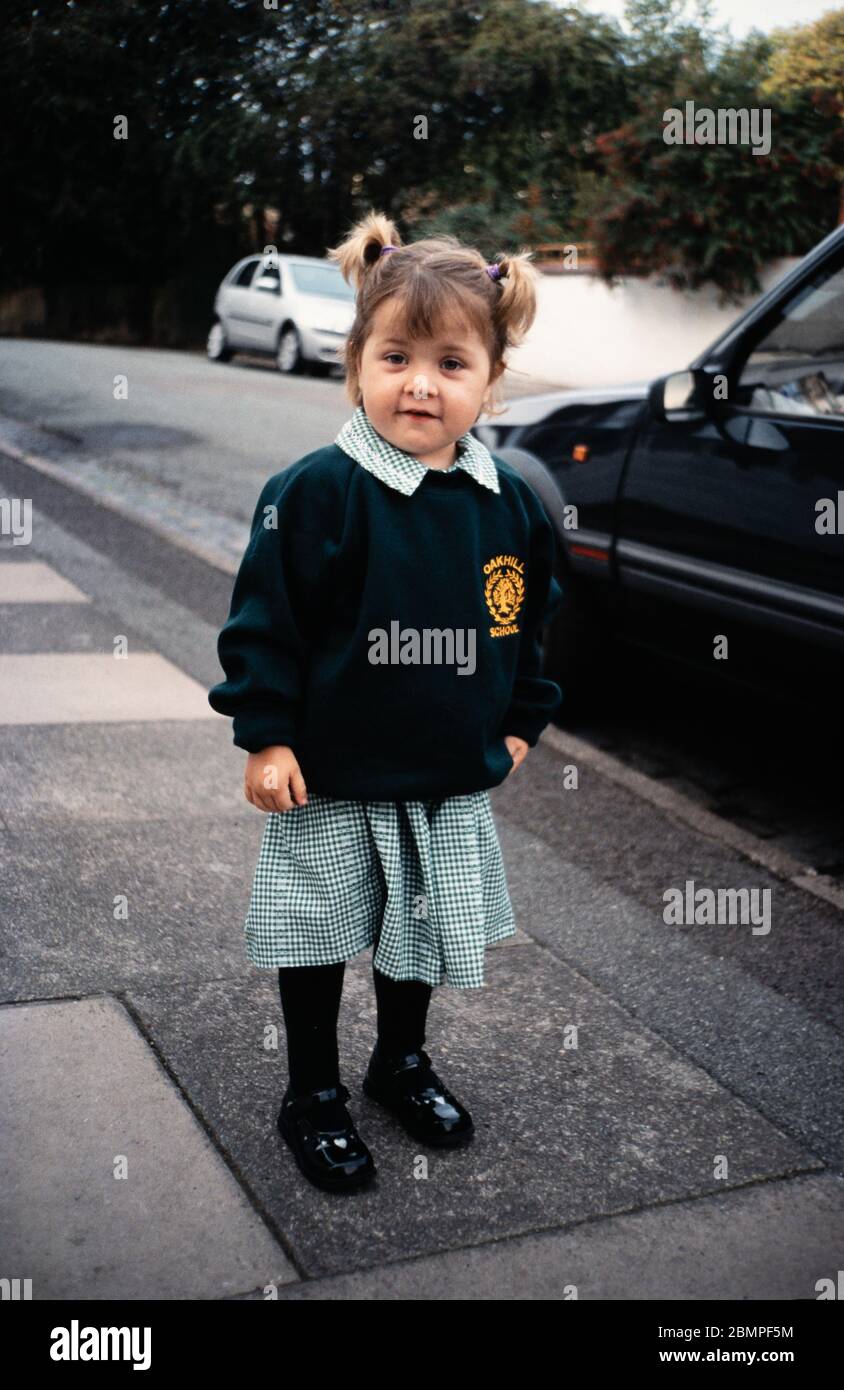 Junge Grundschulkind / Mädchen in einer Wohnstraße, lächelnd in einer grünen Schuluniform, warten auf die Schule gehen, Großbritannien Stockfoto