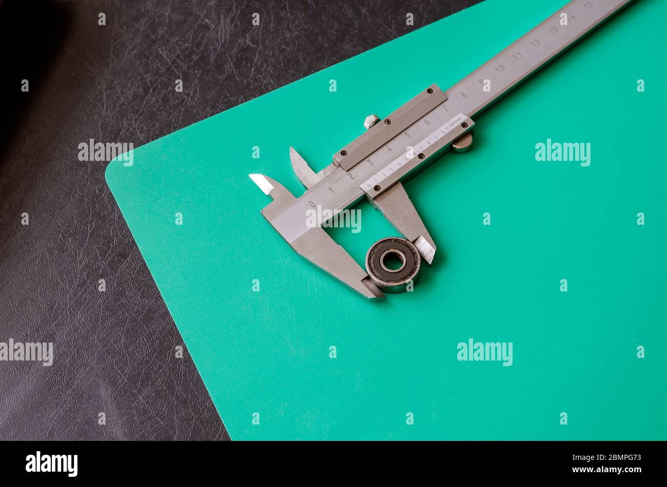 Kugellager und Nonius-Bremssattel auf schwarzem und türkisfarbenem Hintergrund. Messschieber aus Metall mit Dezimalsystem. Berechnung der Maße Stockfoto