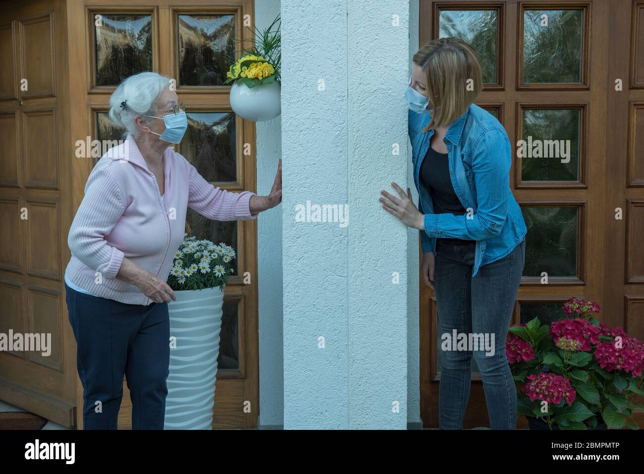 Ältere Frau mit Gesichtsmaske in Haus Quarantäne spricht mit Nachbarn in Sicherheitsabstand Stockfoto