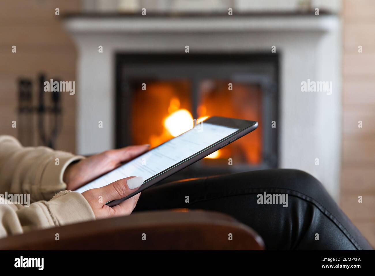 Nahaufnahme einer Frau, die ein digitales Tablet benutzt, Nachrichten liest, soziale Netzwerke durchscrollt, sich in einem Wohnzimmer am Kamin ausgeruht. Entspannen Sie sich zu Hause. Stockfoto