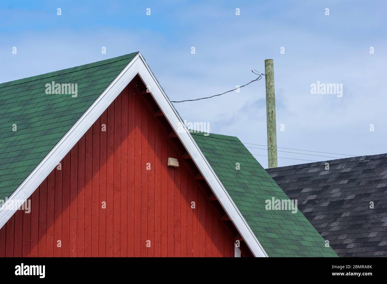 Fisherman's Shack Graphismus. Rot gestrichene Dachziegeln und grüne Dachschindeln. Weiße Giebel Fascia gegen einen blauen Himmel. North Rustico Harbour, PEI, Kanada Stockfoto