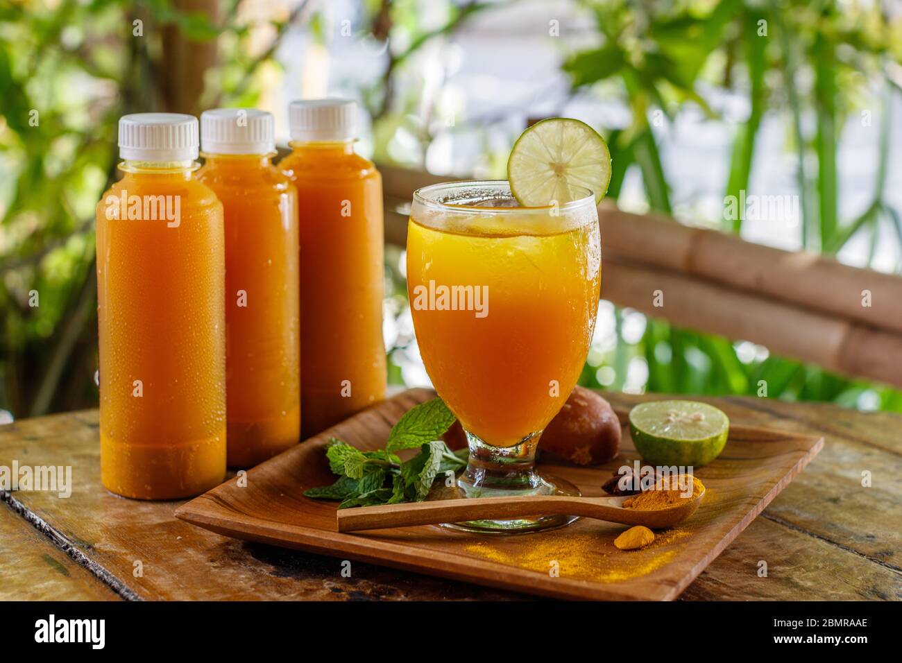 Flaschen und ein Glas Jamu 'Kunir Asam', traditionelle indonesische Kräutermedizin. Serviert mit Limette. Bali, Indonesien. Seitenansicht. Stockfoto