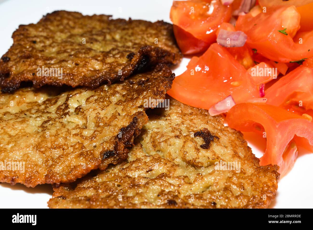 Polnische Kartoffelpfannkuchen mit gehacktem Tomatensalat. Placki Ziemniaczane Rezept Stockfoto