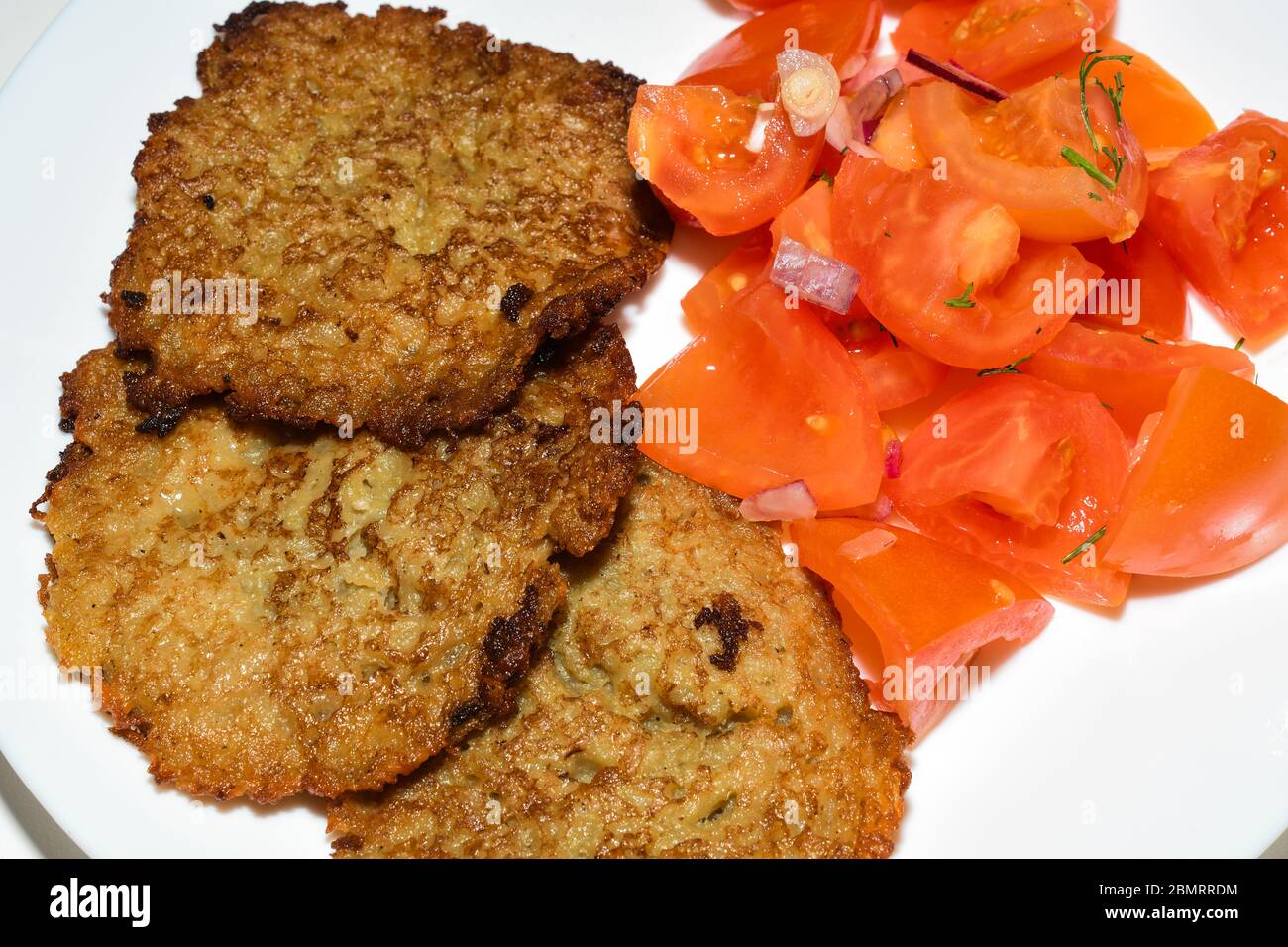 Polnische Kartoffelpfannkuchen mit gehacktem Tomatensalat. Placki Ziemniaczane Rezept Stockfoto