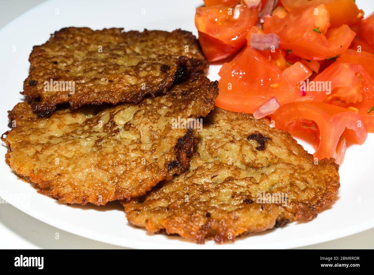Polnische Kartoffelpfannkuchen mit gehacktem Tomatensalat. Placki Ziemniaczane Rezept Stockfoto