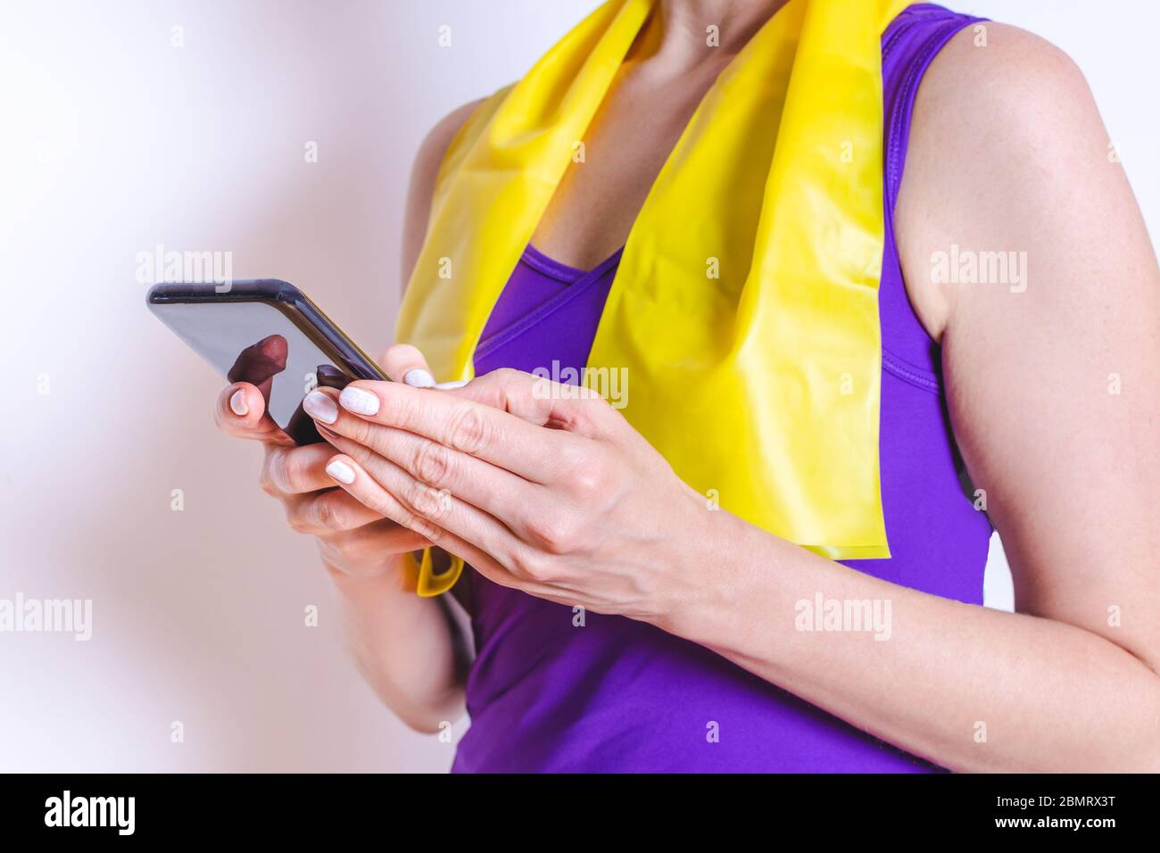 kaukasische Frau Dressing lila Sportbekleidung Überprüfung hier Telefon mit einem elastischen Band um den Hals hängen Stockfoto