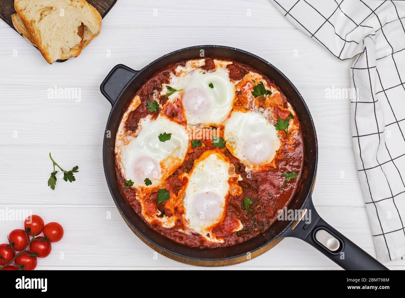 Shakshuka Eiergericht mit Tomatensauce in einer schwarzen Gusseisenpfanne auf dem weißen Holztisch Stockfoto