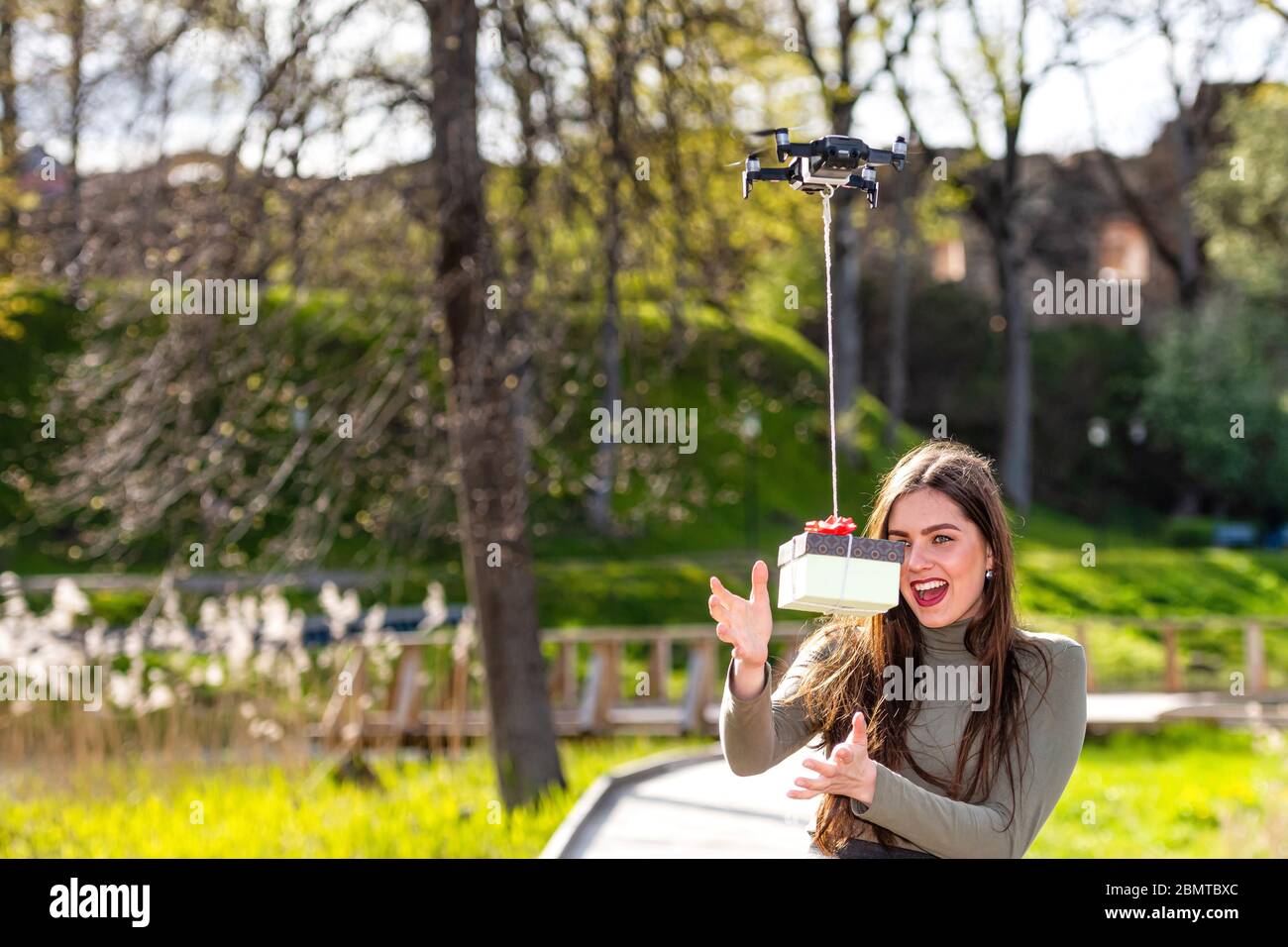 An einem sonnigen und windigen Tag junge lächelnde emotionale Brünette erhält ein Überraschungsgeschenk von Quadcopter, Drohne Lieferservice, Konzept der modernen geliefert Stockfoto