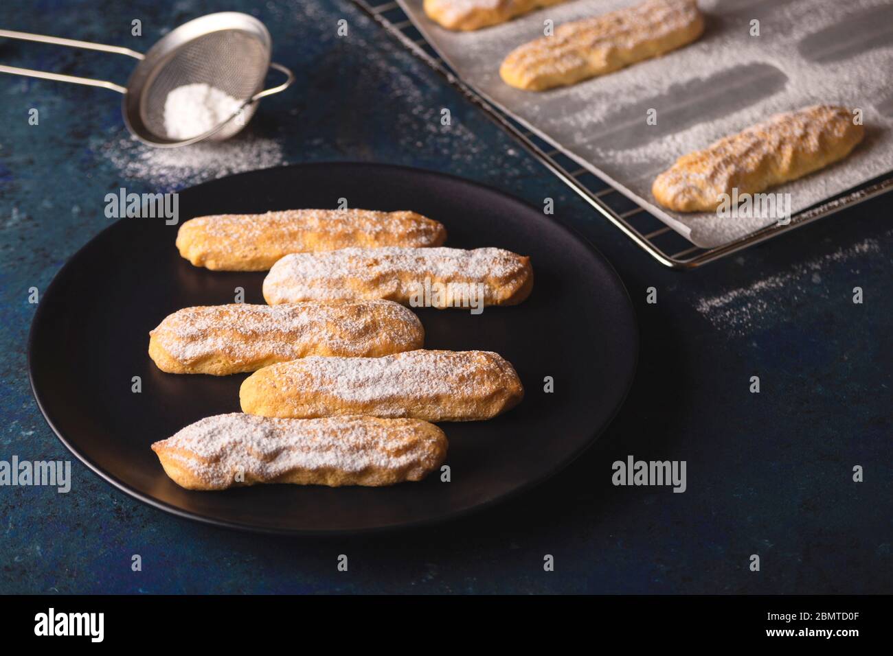 Savoyardi Kekse mit Puderzucker auf blau bestreut Stockfoto