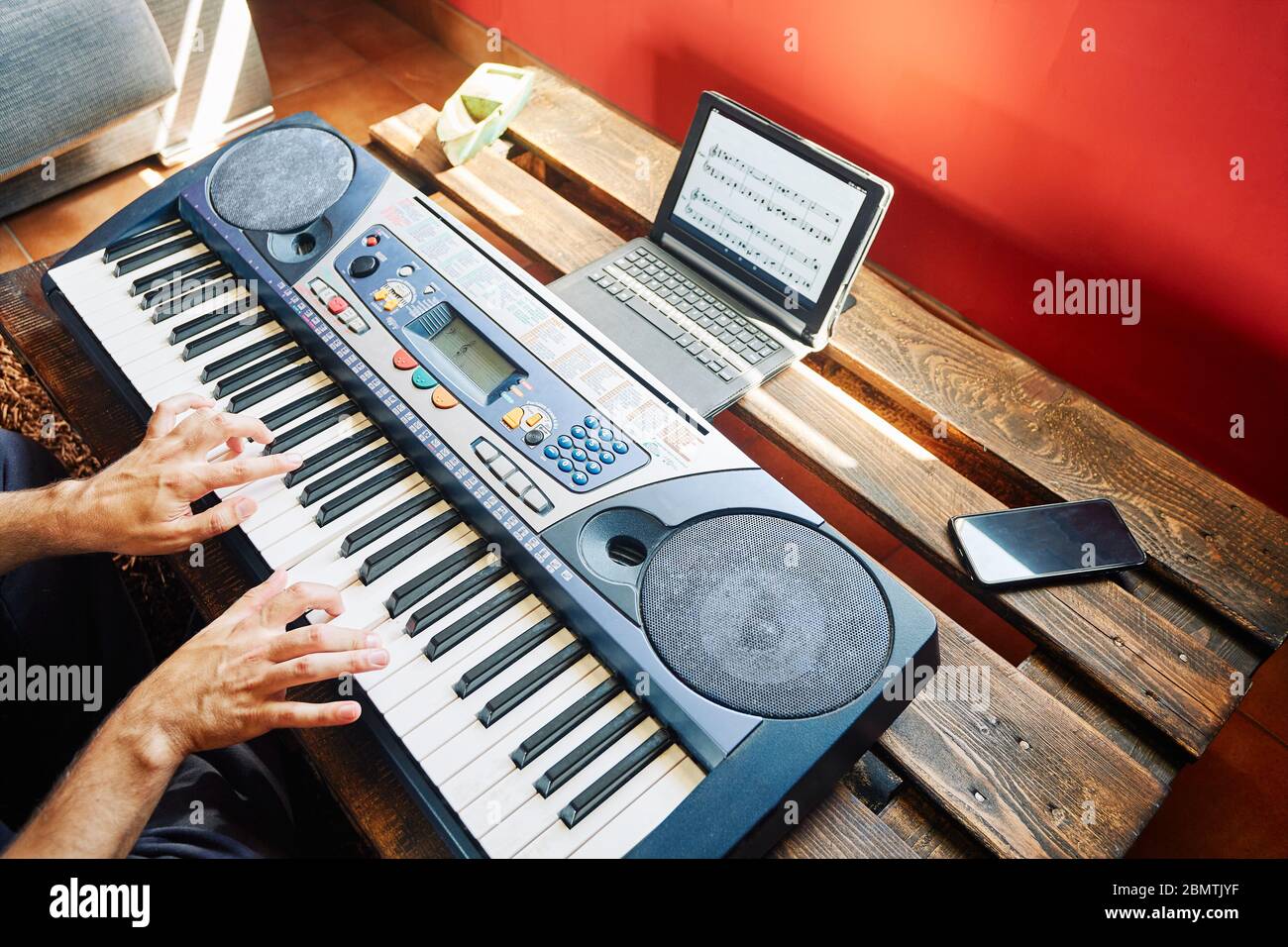 Ein Mann, der zu Hause Klavier spielt, während er ein Tablet benutzt, um die Partituren zu lesen Stockfoto