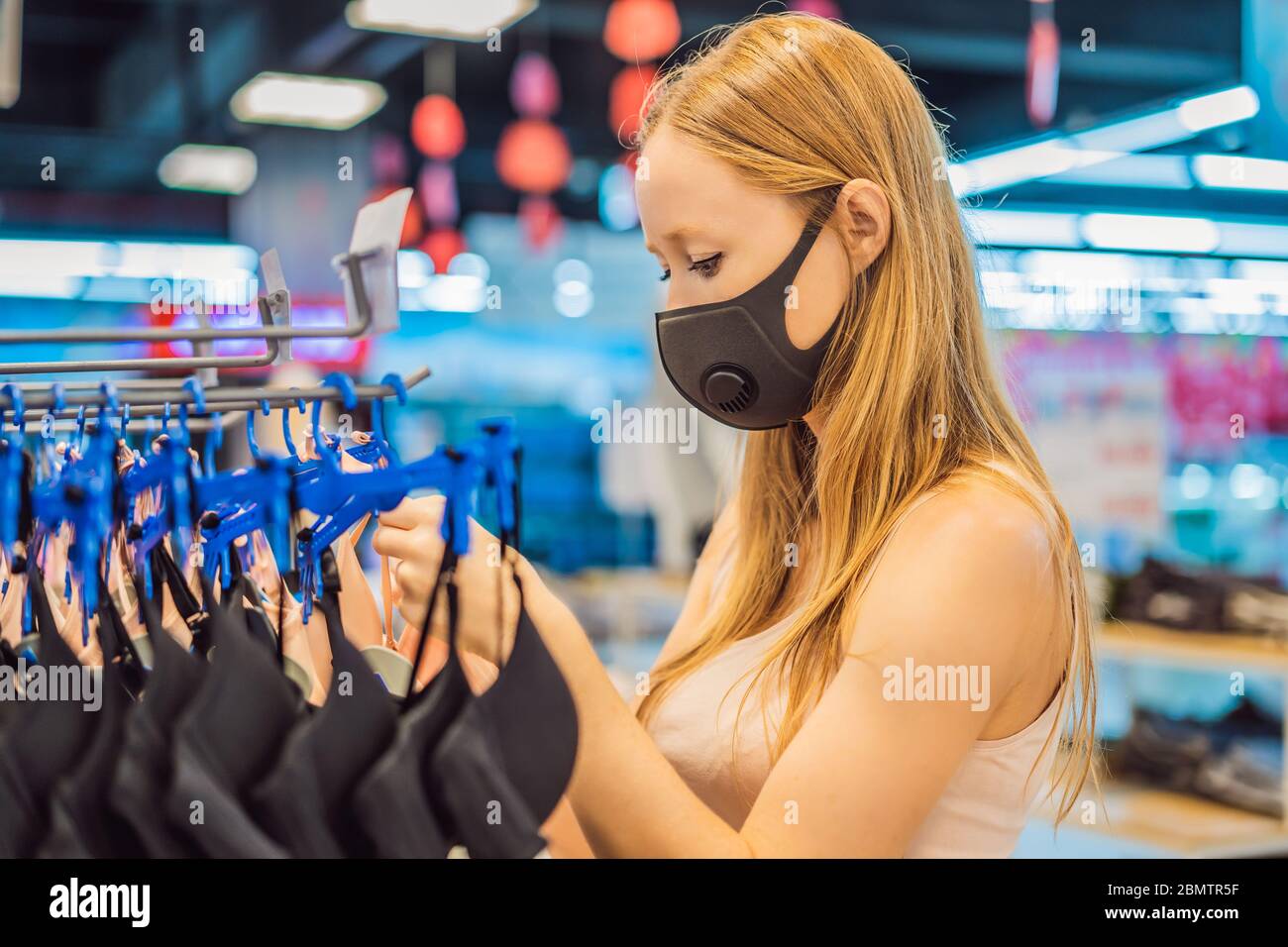 Frau in einem Bekleidungsgeschäft in einer medizinischen Maske wegen eines Coronovirus. Die Quarantäne ist vorbei, jetzt könnt Ihr zum Bekleidungsgeschäft gehen Stockfoto