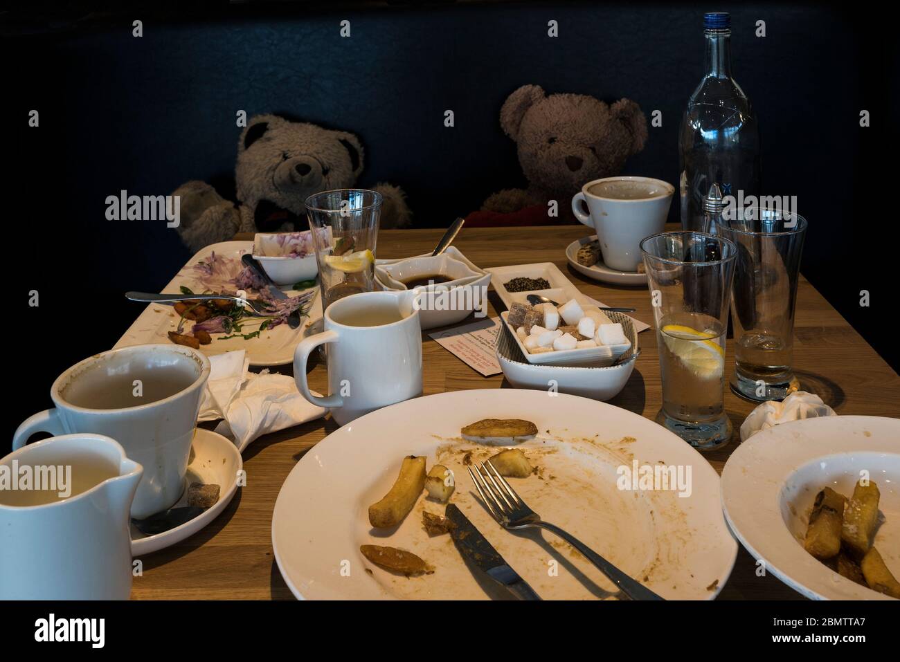 Teddybären auf einem Sitz mit den Resten einer Mahlzeit auf einem Tisch in einem Restaurant. Stockfoto