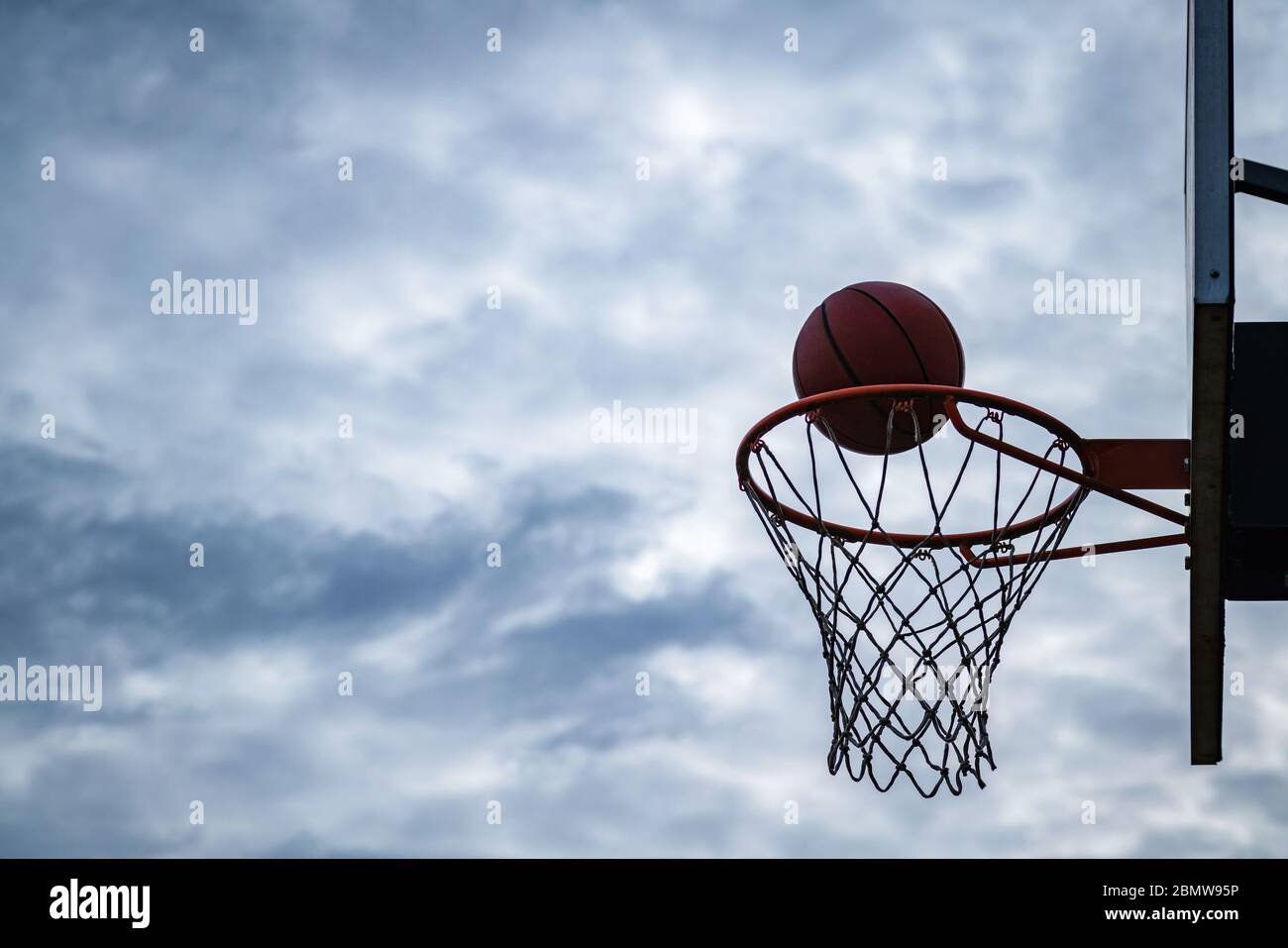 Dunkle Silhouette der Straße Basketball fällt in den Reifen an einem bewölkten Tag. Nahaufnahme eines Balls über dem Netz. Konzept des Erfolgs, Scoring po Stockfoto