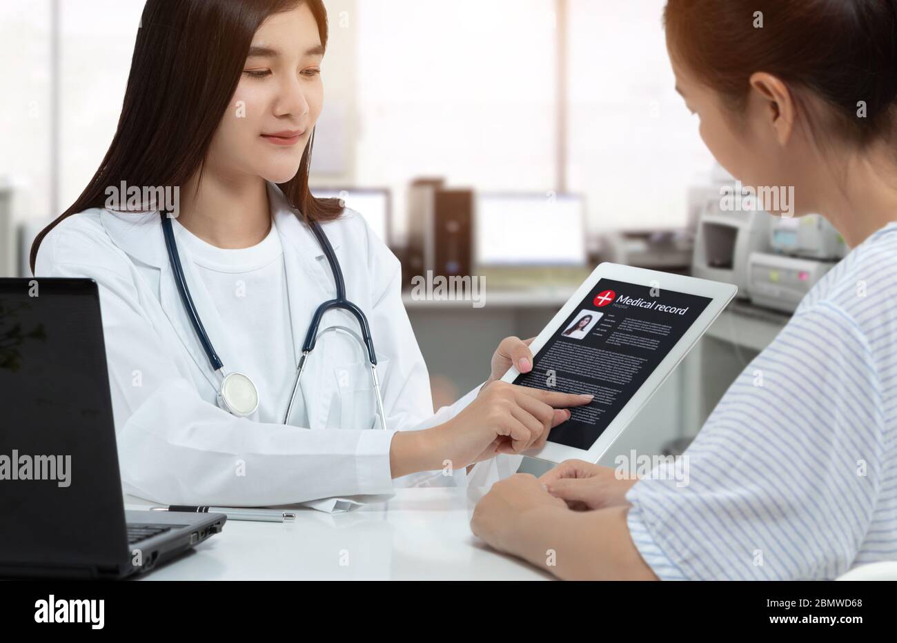 Asiatische Frau Arzt hält Tablette mit Patienten Krankenakte auf dem Bildschirm, während Rücksprache mit Patienten in medizinischen Sprechzimmer. Stockfoto