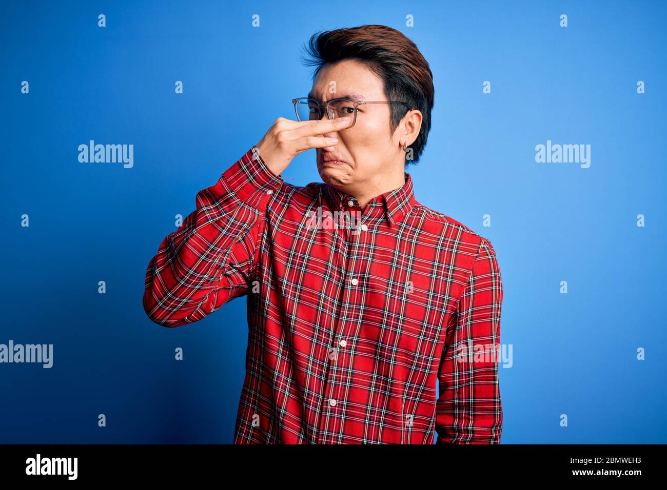 Junger gutaussehender chinese, der lässiges Hemd und Brille auf blauem Hintergrund trägt und