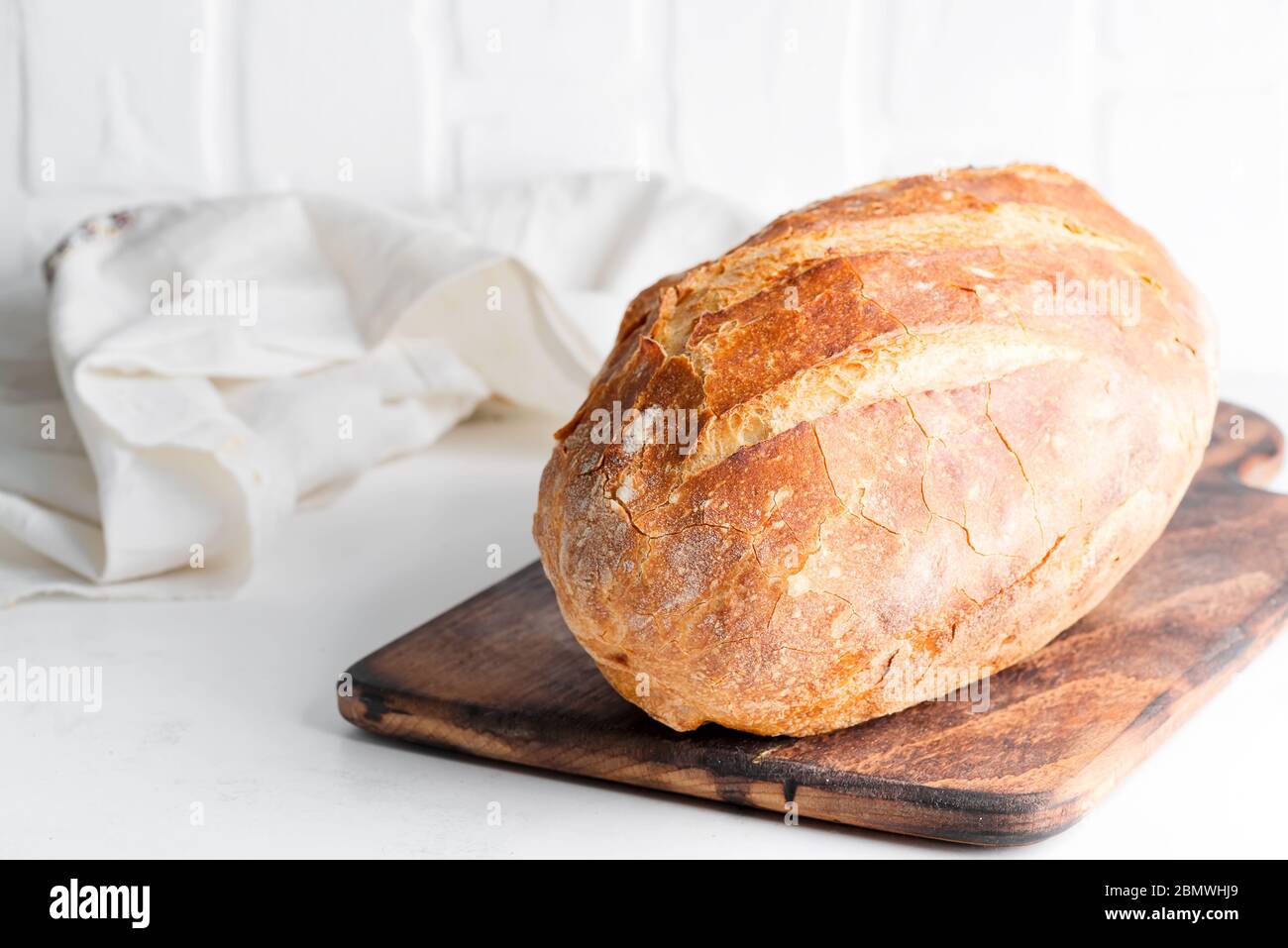 Natürliche hausgemachte frisch gebackenes Laib von weißem knusprigen Brot auf einem Holzbrett und hellgrauen Marmor Hintergrund serviert Textiltuch, kopieren Raum. Oben vi Stockfoto