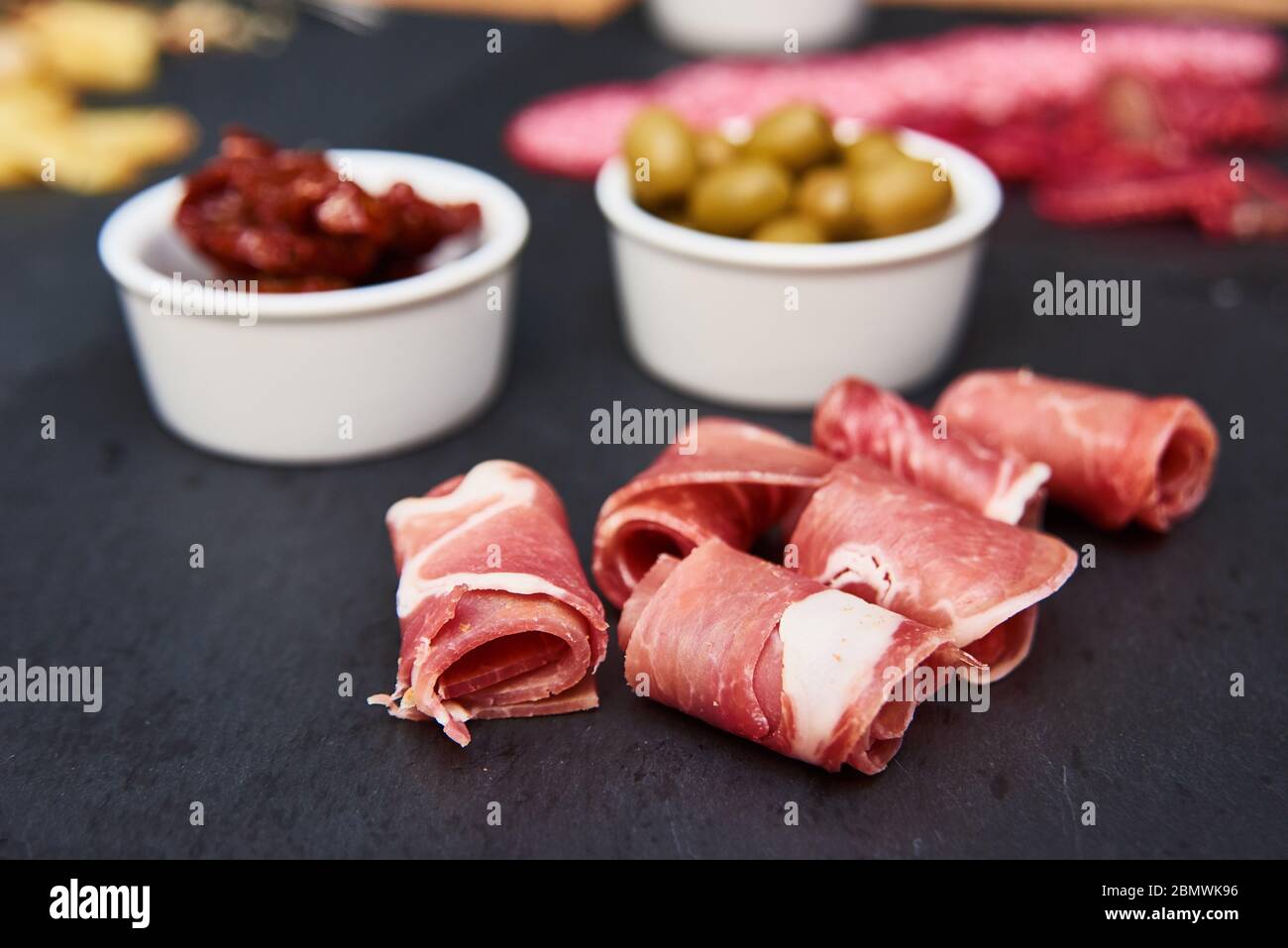 Wurstwaren und grüne Oliven auf Steinschiefer Stockfoto