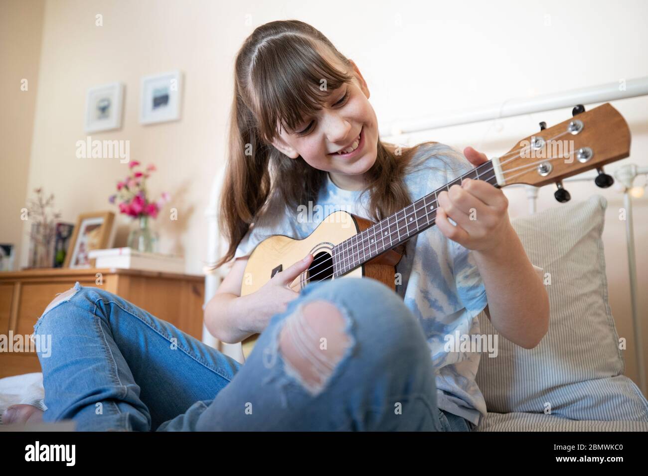 Mädchen Lernen, Ukulele Auf Bett Im Schlafzimmer Sitzen Spielen Stockfoto