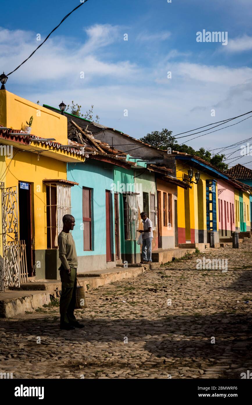 Mann, der in einer typischen Kopfsteinpflaster-Straße mit bunten Häusern im Kolonialzeitzentrum der Stadt, Trinidad, Kuba, steht Stockfoto