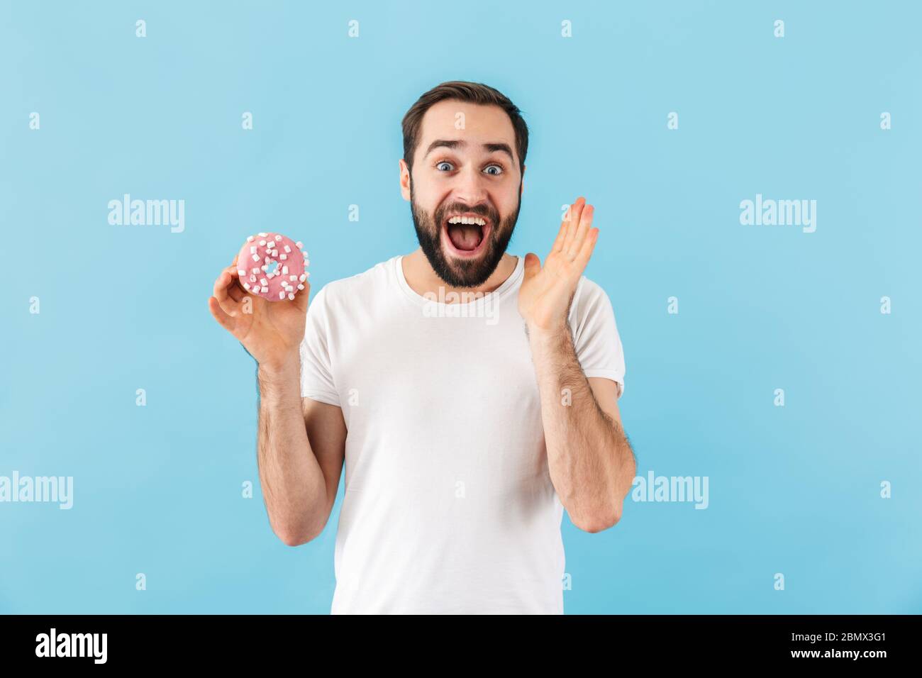 Bild von jungen emotional aufgeregt Mann isoliert über blauen Wand Hintergrund halten Donut. Stockfoto