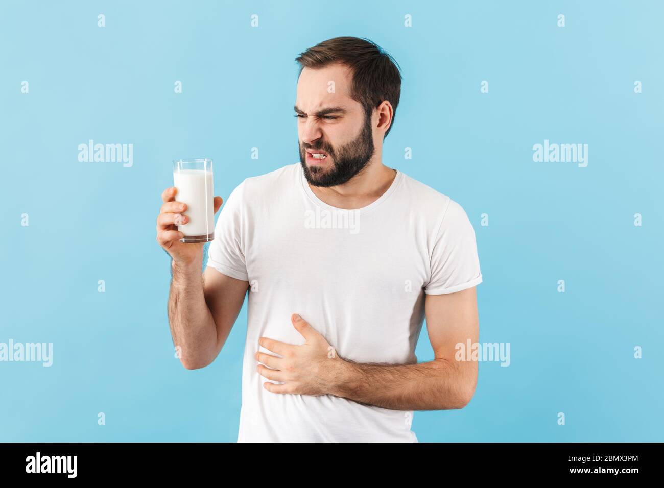 Bild von jungen unzufrieden Mann mit Magenschmerzen isoliert über blauen Wand Hintergrund hält Milch. Stockfoto