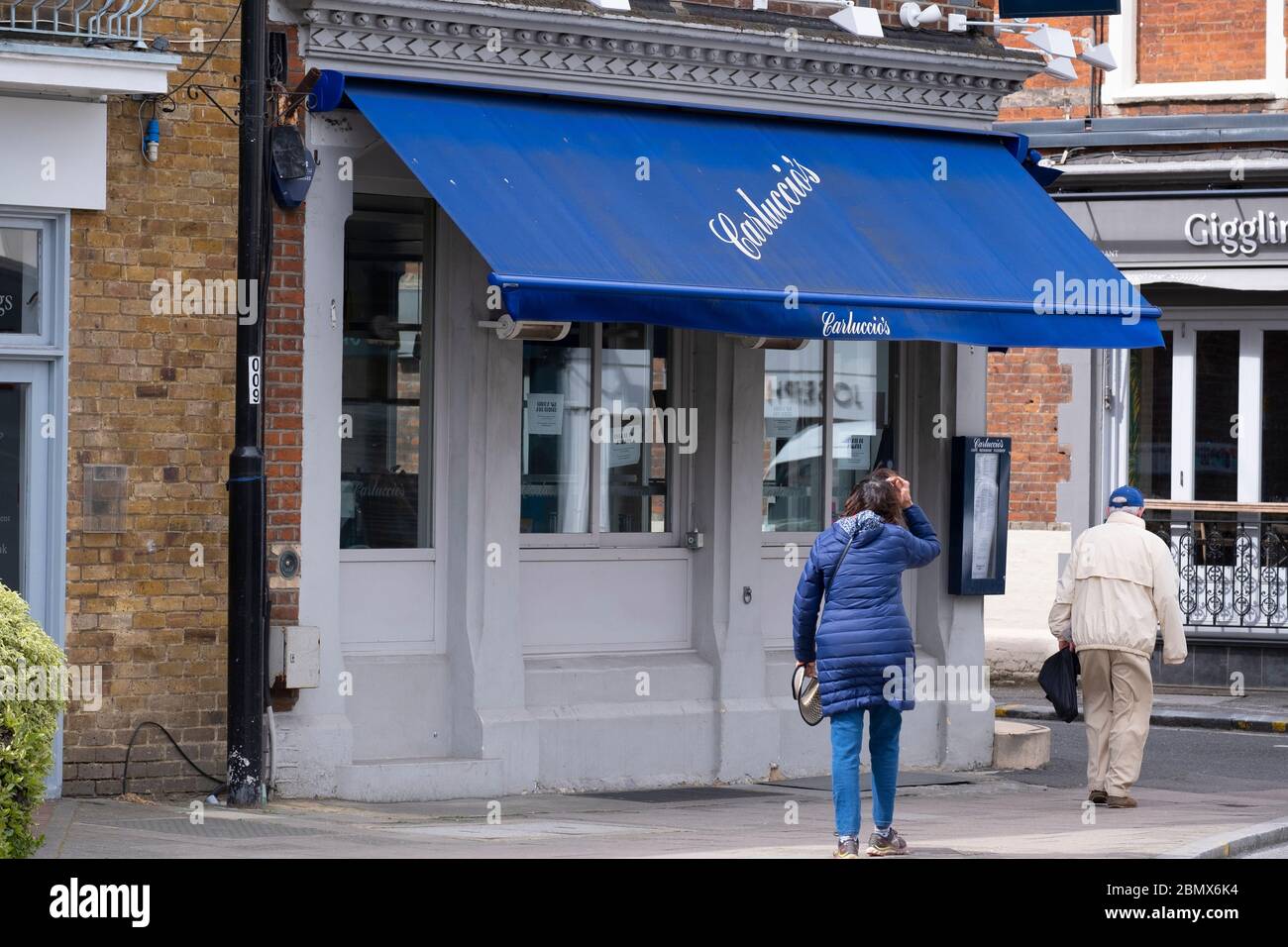 Wimbledon, London, Großbritannien. 11 Mai 2020. Ruhige Hauptstraße in Wimbledon Village. Dieser Bereich würde normalerweise für die 2020 Wimbledon Tennis Championships vorbereiten, die während der Coronavirus Pandemie abgesagt wurden. Zwei Fußgänger gehen am Restaurant Carluccios vorbei, die Kette fiel in die Verwaltung und ein Käufer wird derzeit gesucht. Quelle: Malcolm Park/Alamy Live News. Stockfoto