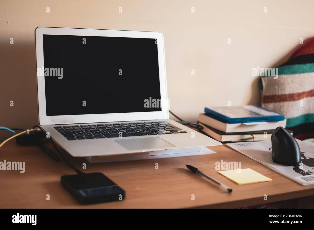 Unkonventioneller Home Office-Schreibtisch für die Arbeit von zu Hause aus. Der Laptop wird von Büchern angehoben und ein Magazin wird als Mäusematte verwendet. Stockfoto