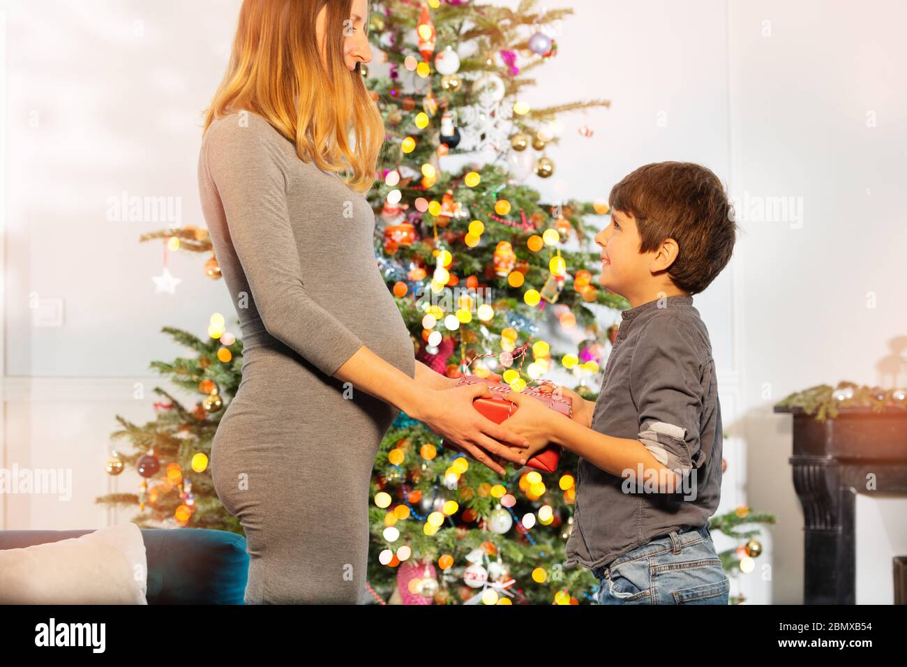 Schwangere Mutter Geschenk zu Sohn, Junge stehen in der Nähe von Neujahr Baum und Kamin Stockfoto