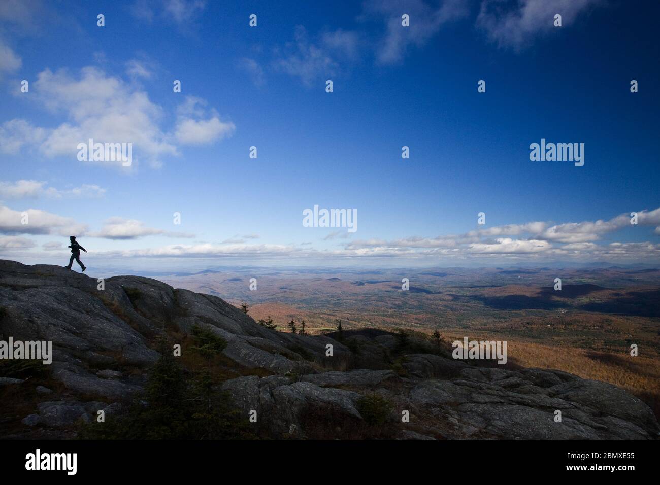 Ein Wanderer, der vor einem herbstlichen Himmel mit der Vermont-Landschaft im Hintergrund silhouettiert, macht einen kleinen Schritt Stockfoto