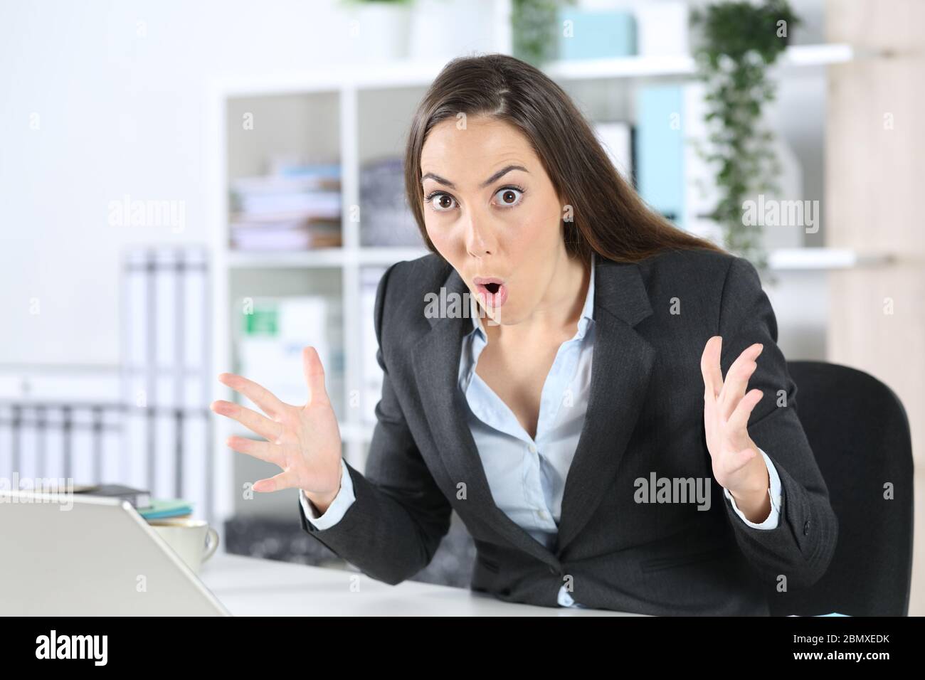Eine überraschte Geschäftsführerin, die überrascht auf die Kamera schaut, die auf ihrem Schreibtisch im Büro sitzt Stockfoto
