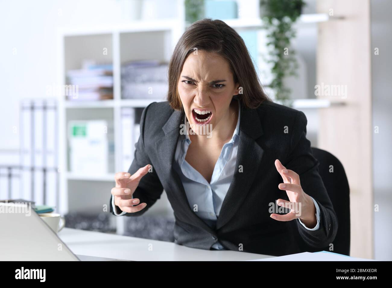 Wütende Exekutive Frau, die auf Kamera schaut, die auf ihrem Schreibtisch im Büro sitzt Stockfoto