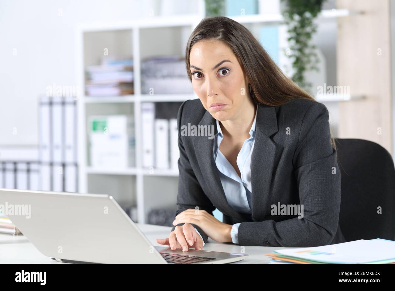 Verwirrte Exekutive Frau mit Laptop, die auf der Kamera auf ihrem Schreibtisch im Büro sitzt Stockfoto