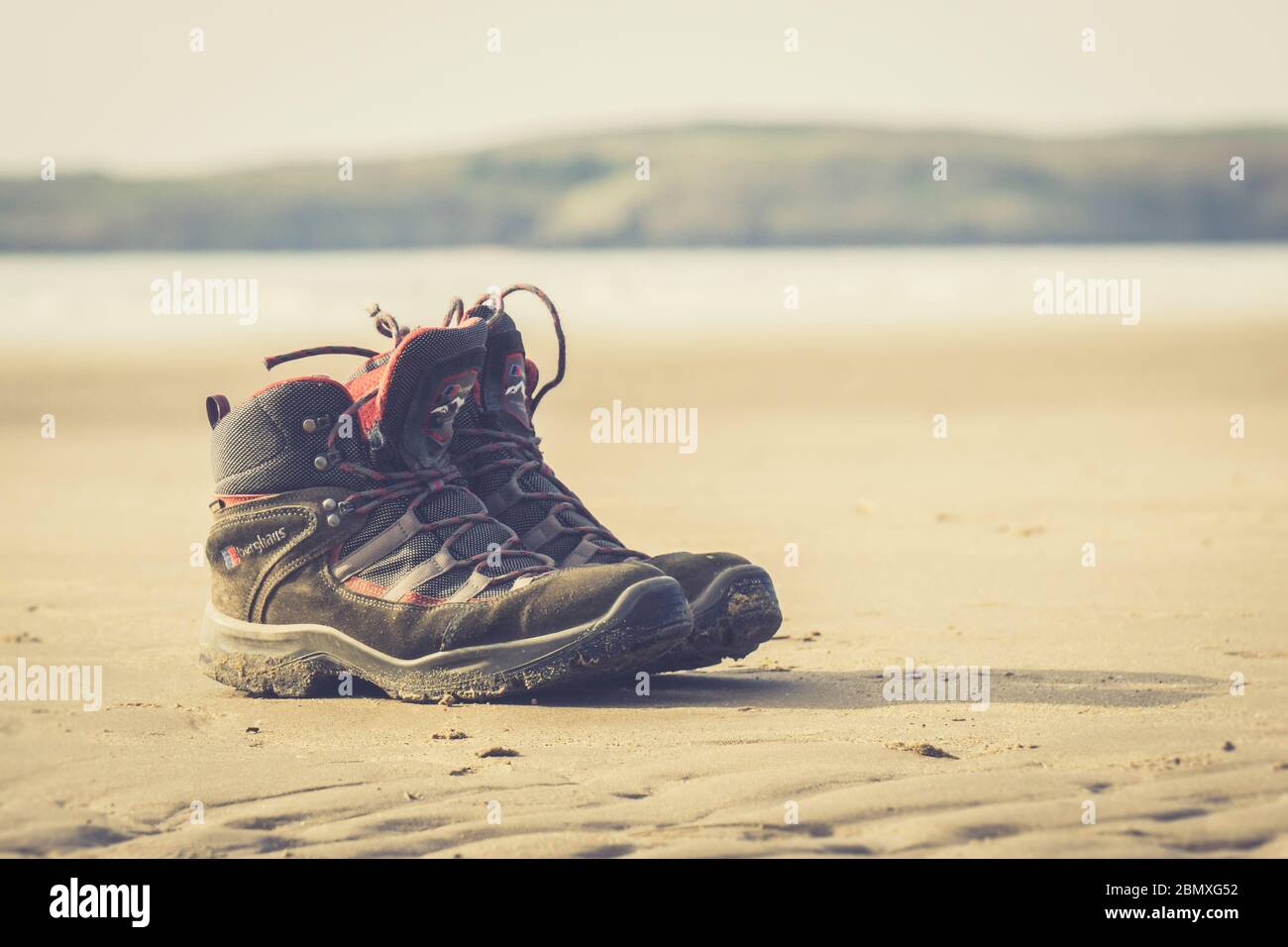 Nahaufnahme von verlassenen Wanderschuhen für Männer, isoliert auf Sand eines leeren, menschenleeren Strandes in der Sommersonne, Newborough Beach, Anglesey, North Wales, Großbritannien. Stockfoto