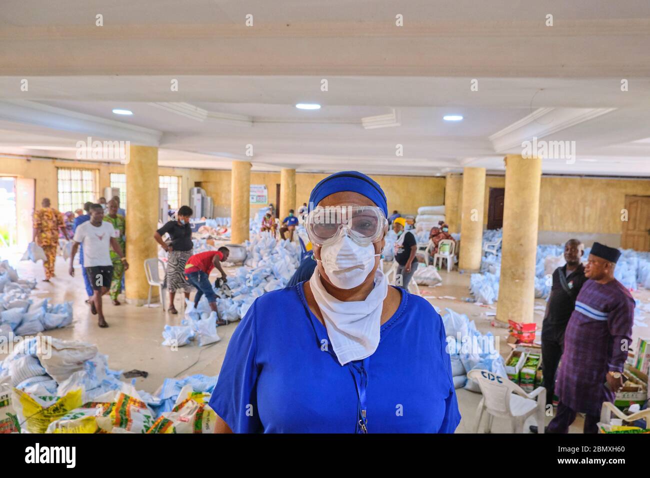 Ein Leiter des Gemeinderats posiert für ein Foto, während Reissäcke und andere Gegenstände während der Covid-19-Sperre in Lagos, Nigeria, als Palliativmittel verpackt werden. Stockfoto