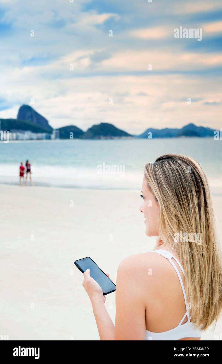Eine junge Frau, die ihr Handy am Strand in Rio benutzt Stockfoto