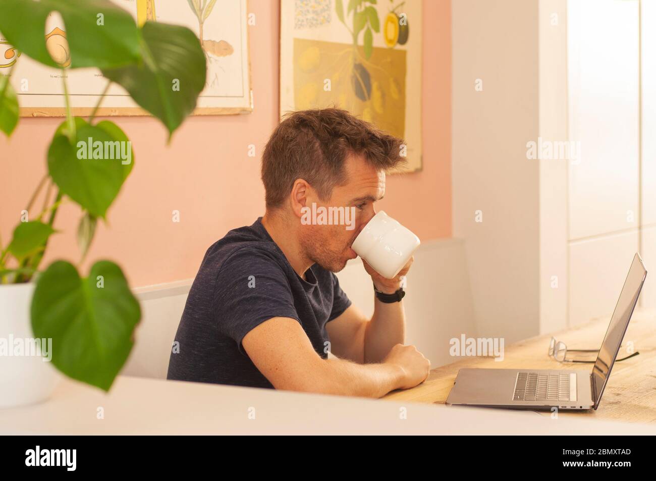 Porträt eines Mannes, der von zu Hause auf einem Laptop-Computer während der Coronavirus-Sperre arbeitet, Kaffee trinkt. Querformat. Stockfoto