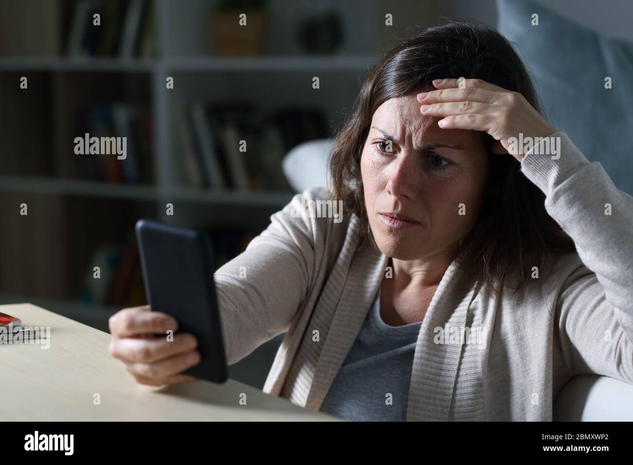 Besorgte Erwachsene Frau liest schlechte Nachrichten auf Smartphone sitzt auf dem Boden in der Nacht zu Hause Stockfoto