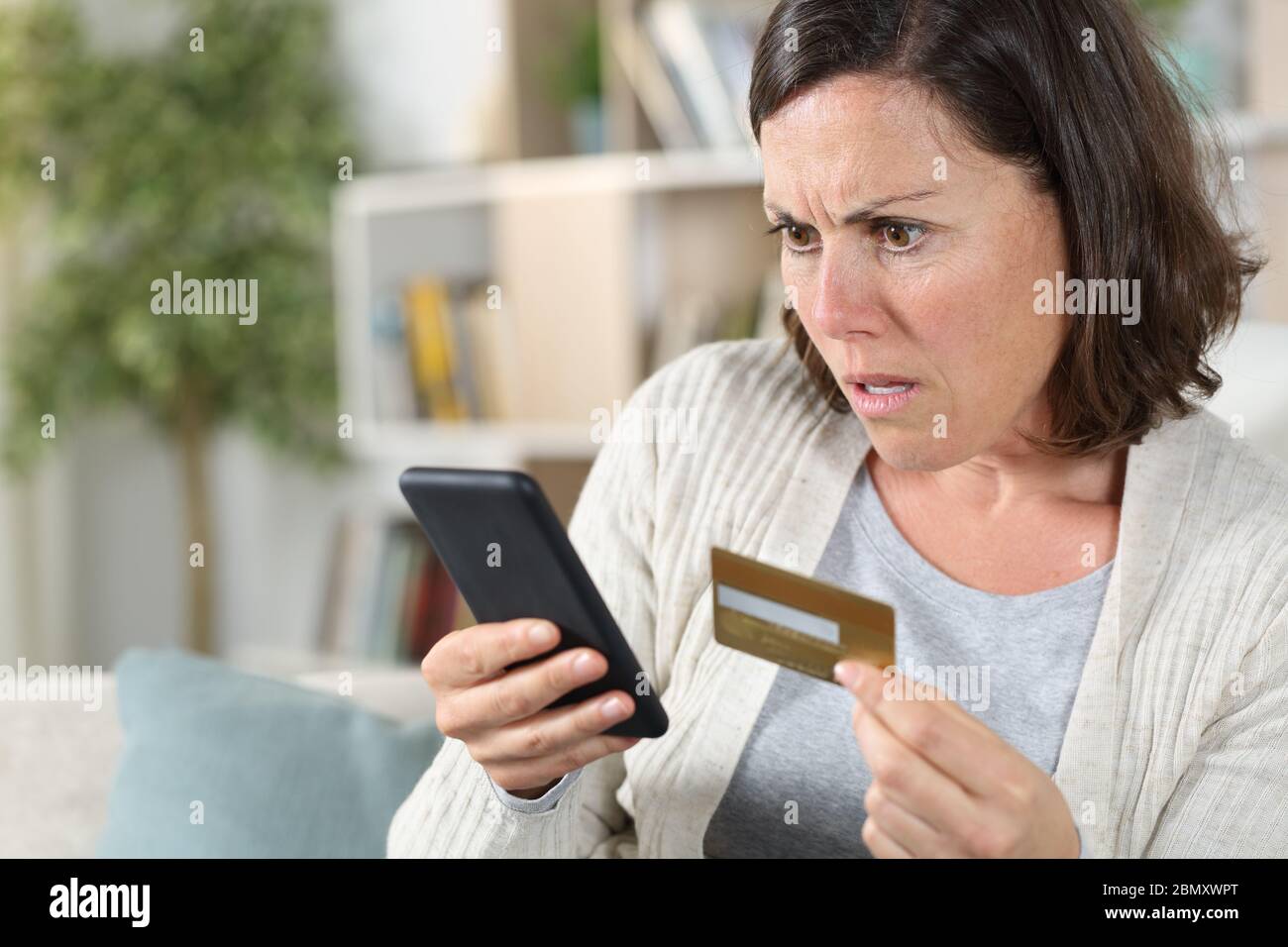 Besorgte Erwachsene Frau online zahlen auf Smartphone mit Kreditkarte sitzt auf dem Sofa zu Hause Stockfoto